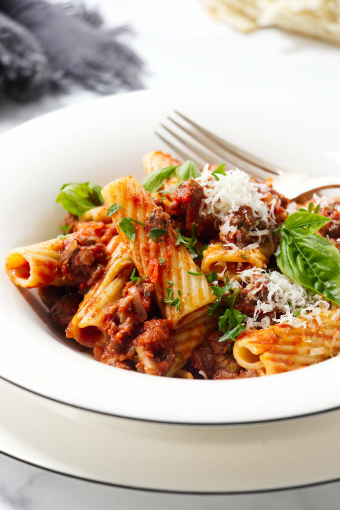 Sausage rigatoni in a pasta bowl topped with basil.