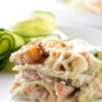 Creamy seafood lasagna slice with shrimp and salmon on a white plate.