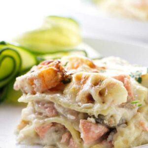 Creamy seafood lasagna slice with shrimp and salmon on a white plate.