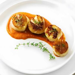 Four seared scallops on orange sauce, garnished with herbs and thyme.