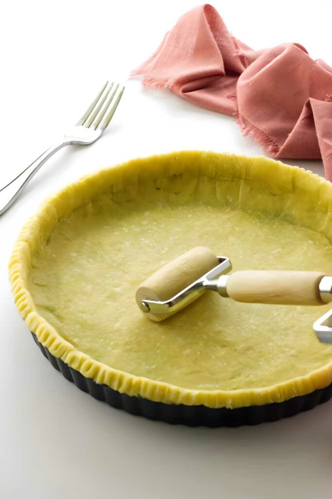 Unbaked pie crust in tart pan, rolled flat with small wooden rolling pin.