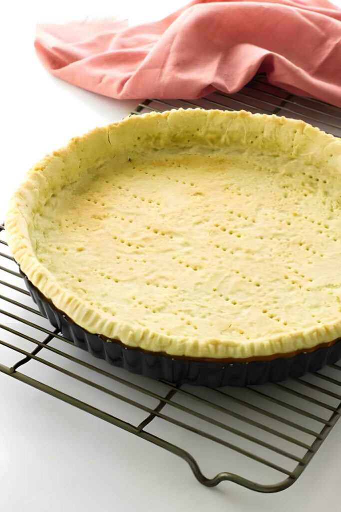 Golden baked pie crust in tart pan on cooling rack, pink cloth behind.