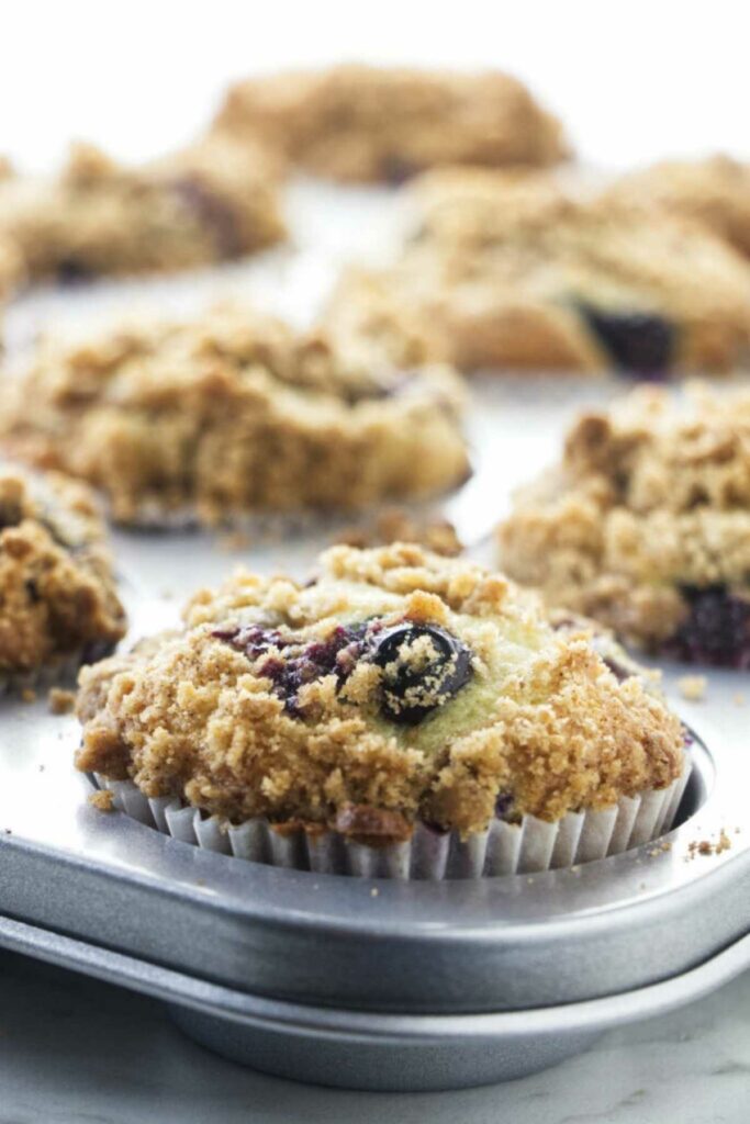 Close-up of a blueberry muffin with streusel topping in a muffin tin.