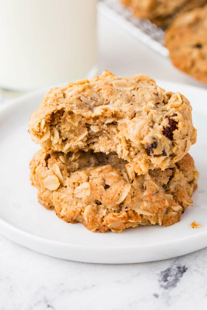 Two oatmeal cookies on a plate with a bite taken from one.