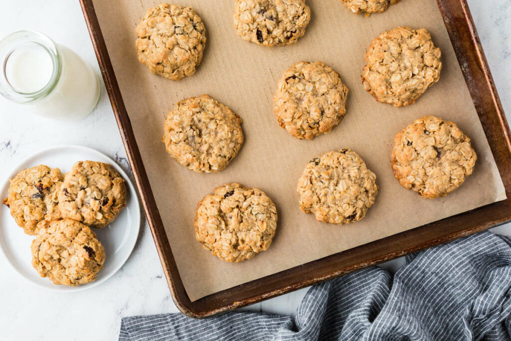 Several oatmeal cookies on a cookie sheet next to a glass of milk.