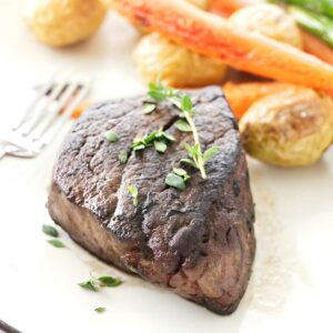 Cooked steak with herbs, roasted potatoes, carrots, and asparagus on plate.