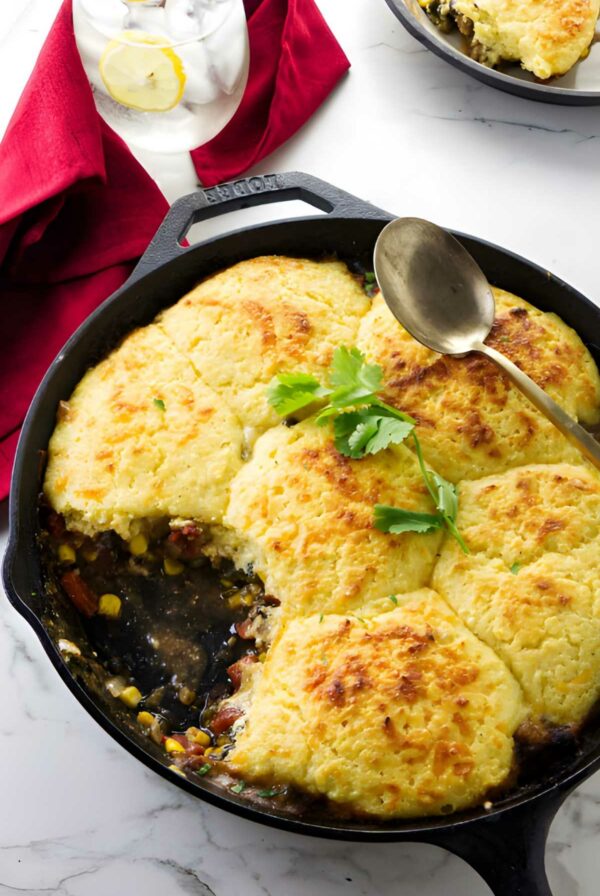 Savory pork skillet pie with golden biscuits in cast iron skillet, vegetables visible, parsley garnish.
