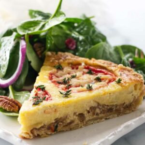 Quiche slice with herbs and tomatoes, served with spinach salad.