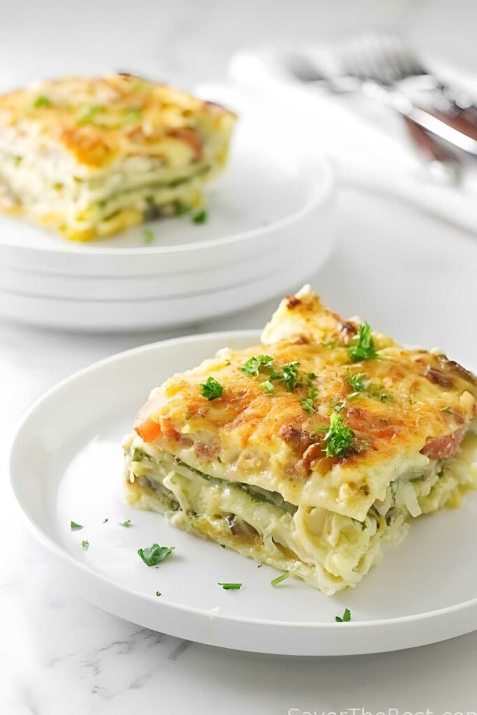 Vegetable lasagna slice with parsley on white plate.