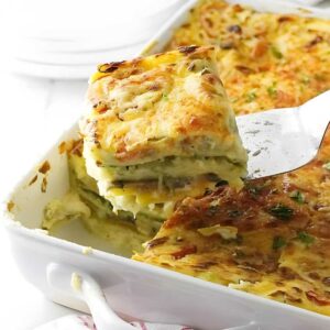 Vegetable lasagna being served from a white dish, golden cheese on top.