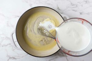 Whisking warm milk into a flour and butter roux.