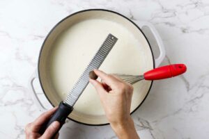 Grating fresh nutmeg into bechamel sauce.