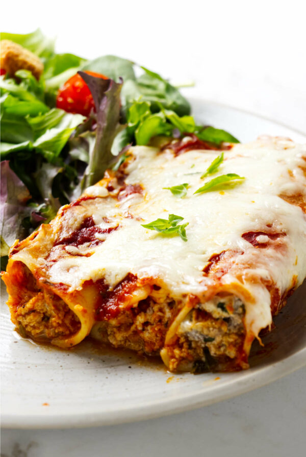 Three filled pasta tubes on a plate with a salad.