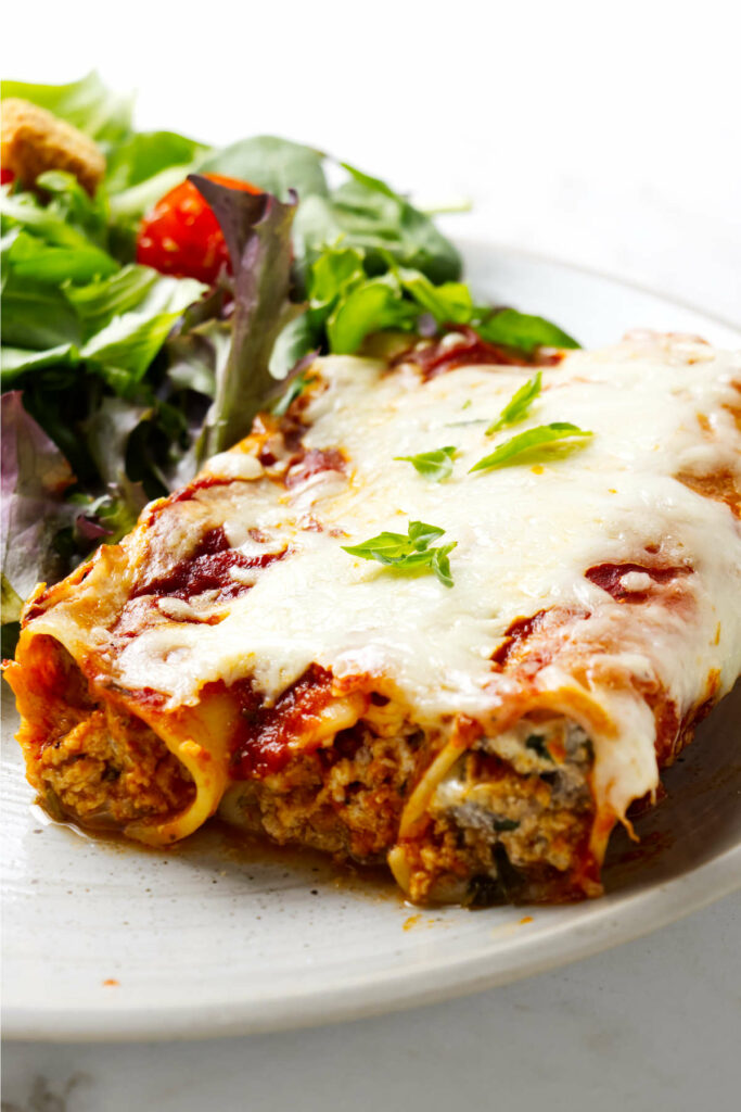 Three filled pasta tubes on a plate with a salad.