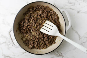 Browning ground beef in a white skillet.
