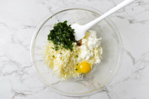 Combining cheese with herbs and eggs in a bowl.