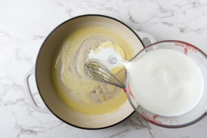 Adding milk to the roux mixture.