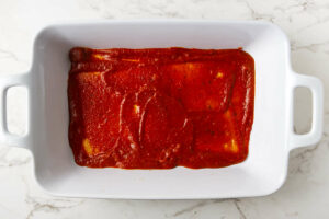Spreading marinara sauce in a baking dish.