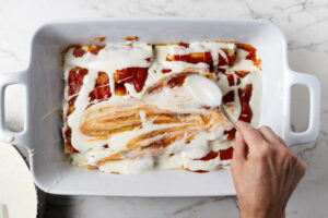 Adding bechemel sauce to the top of the cannelloni.