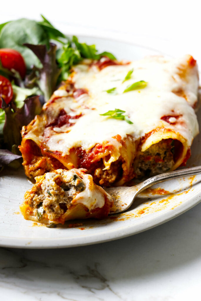 Three cheesy beef filled cannelloni on a dinner plate with a salad.