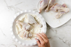 Coating chicken drumsticks in seasoned flour.