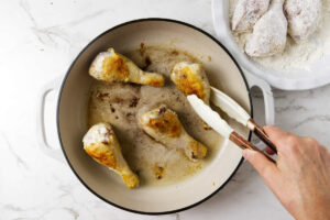 Browning chicken legs in a skillet.