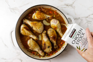 Adding chicken broth to the pan with the chicken legs.
