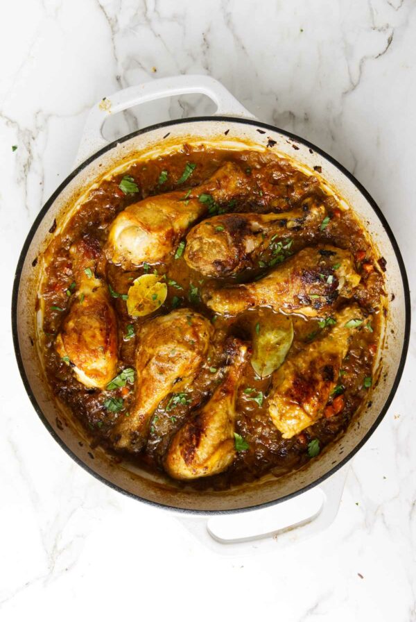 A large skillet filled with braised chicken legs and herbs.