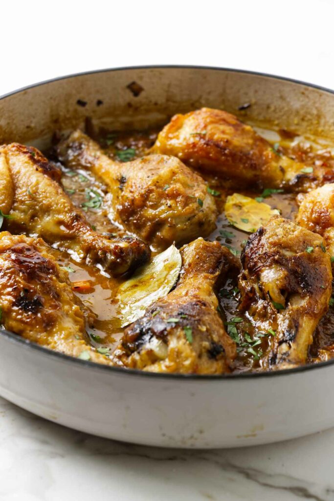 Braised chicken drumsticks in a large pan with sauce.