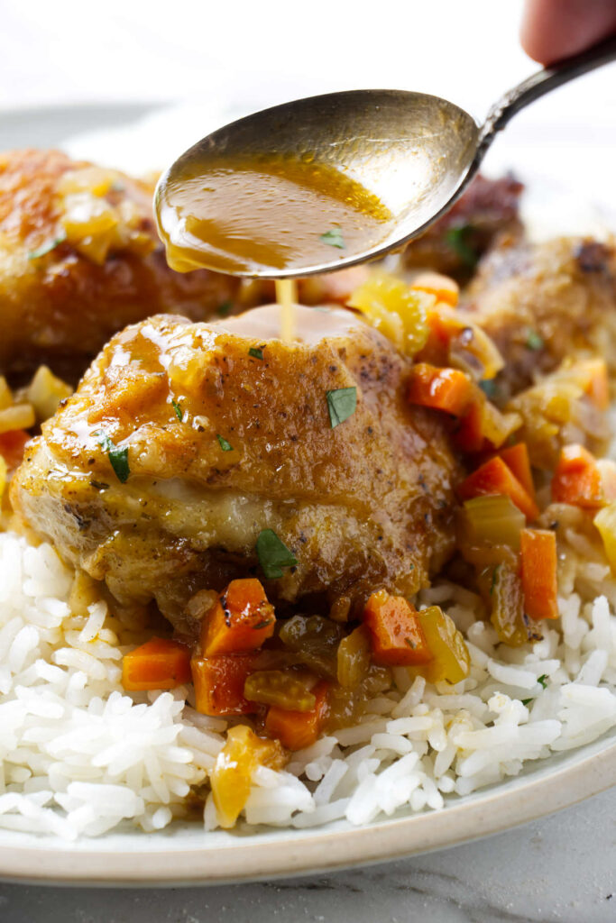 Spooning sauce over a chicken leg on a bed of rice.