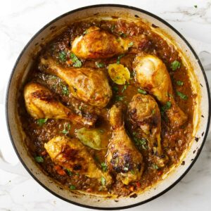 A large skillet filled with seven braised chicken legs in sauce.