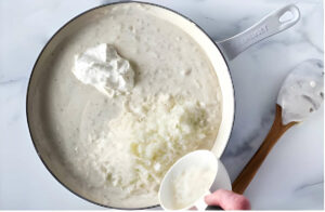 Adding cheese to the white lasagna sauce.