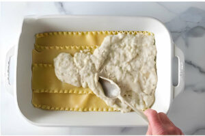 Spreading a white sauce over lasagna noodles.