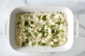 Adding basil and herbs to a layer of mushroom lasagna.