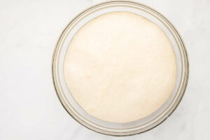 Pizza dough proofing in a glass bowl.
