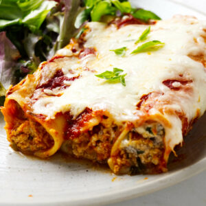 Three cannelloni pasta filled with beef and cheese next to a salad.