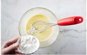 Whisking cornstarch and flour into an egg yolk mixture.