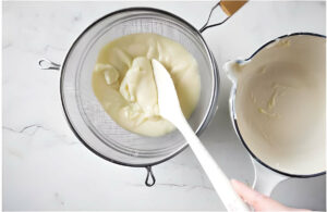 Straining the pastry cream through a metal sieve.