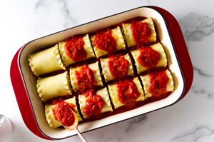 Spooning sauce on top of lasagna rolls.