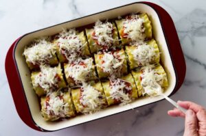 Adding shredded cheese on top of Lasagna roll-ups.