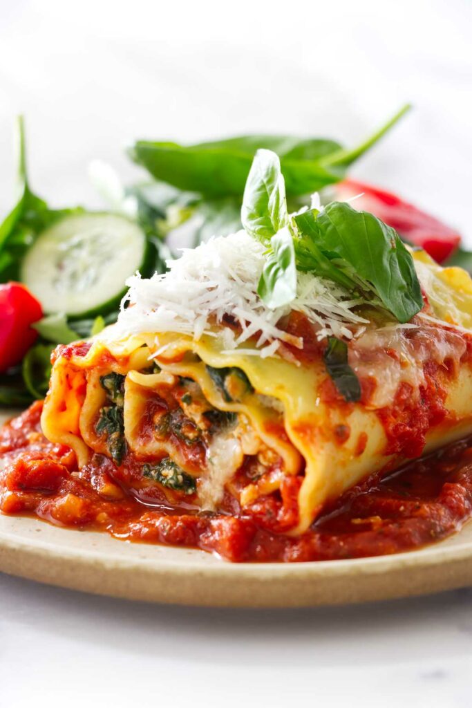 A lasagna roll up on a plate with a garden salad.