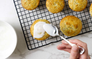 Spooning lemon glaze on top of poppy seed muffins.