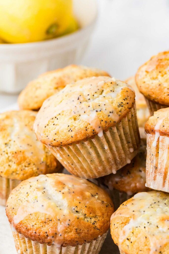 A pile of sourdough lemon poppy seed muffins in front of a bowl of fresh lemons.