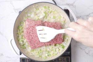 Adding sausage and beef to a skillet.
