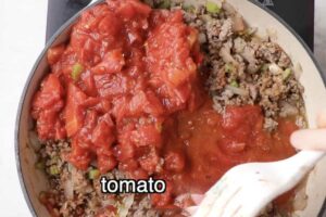 Adding tomato sauce and tomatoes to the meat mixture.