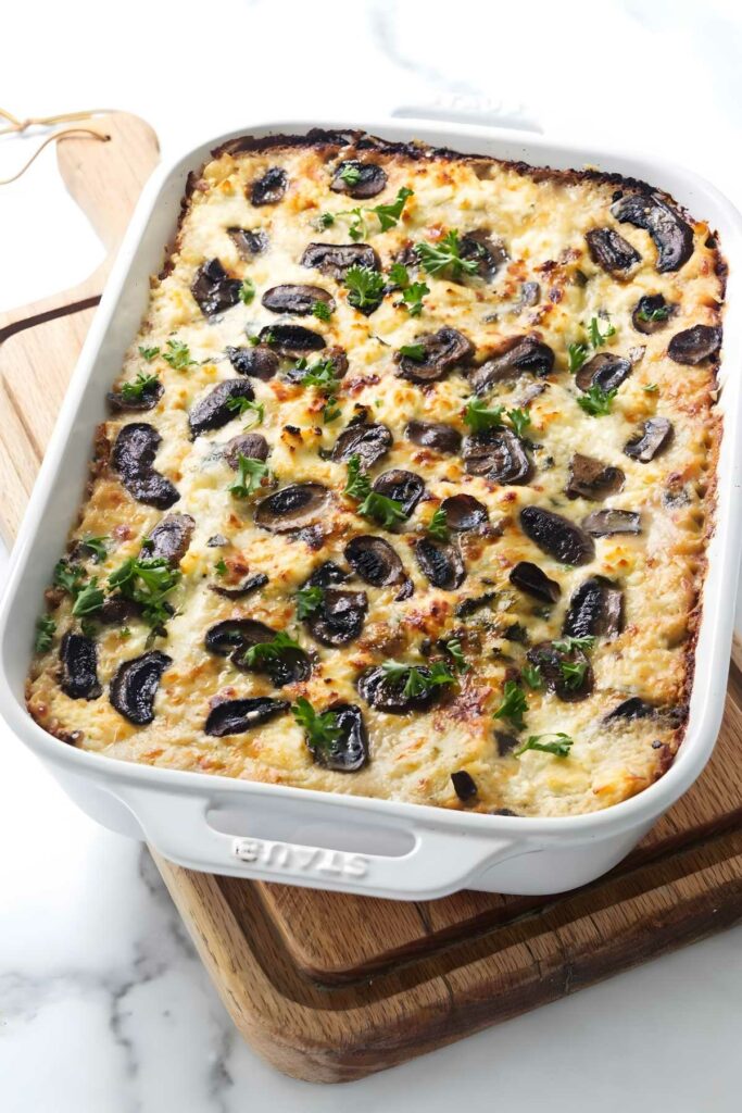 Baked casserole with melted cheese, mushrooms, and parsley in a white dish.