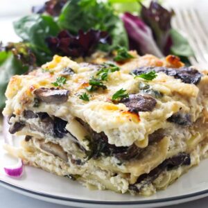 Creamy mushroom lasagna slice with herbs and mixed salad on a plate.
