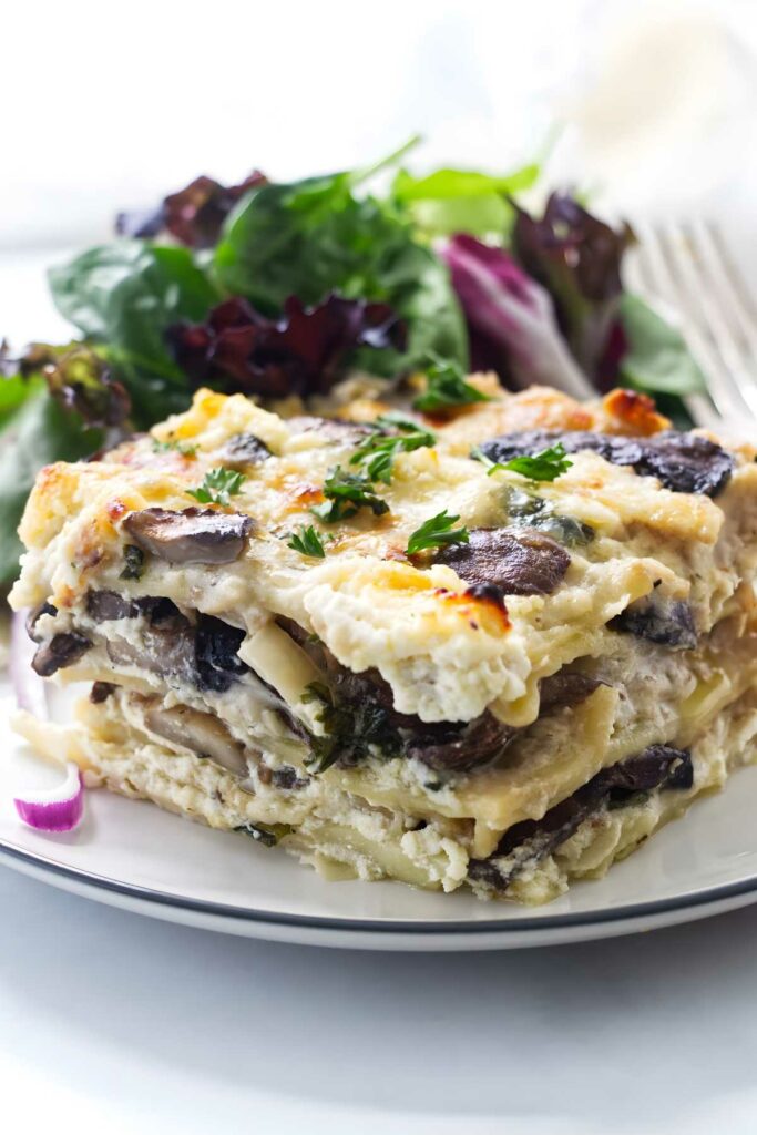 Creamy mushroom lasagna slice with herbs and mixed salad on a plate.