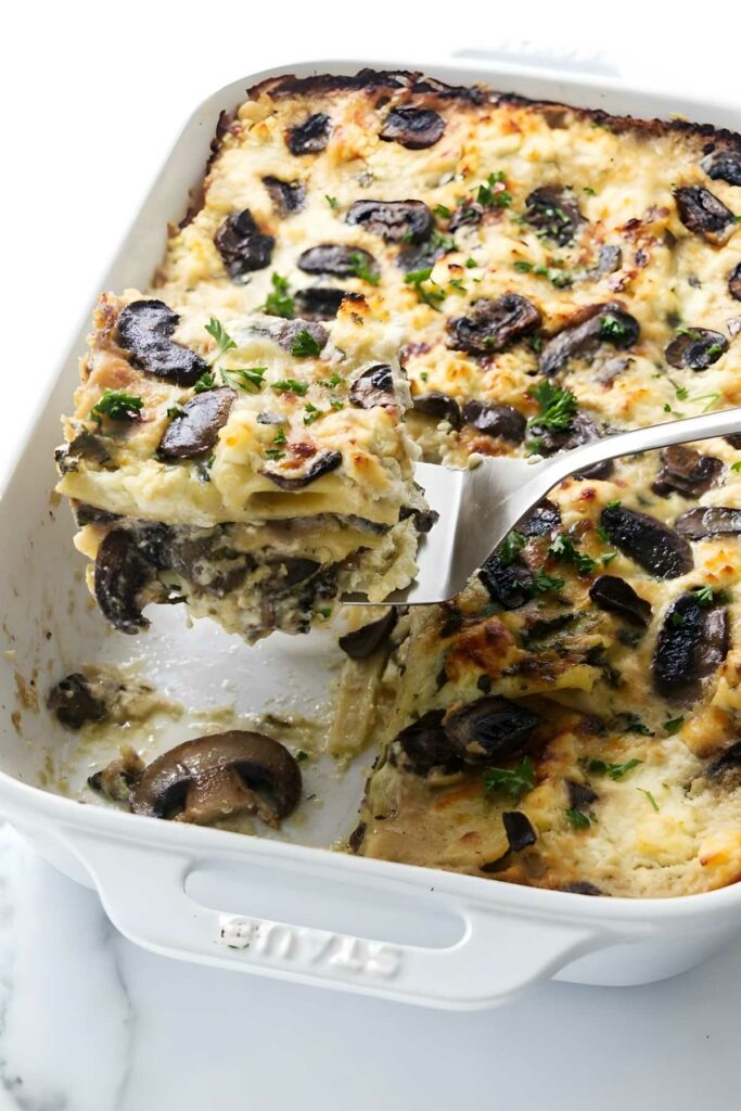 White mushroom lasagna in a dish, slice lifted with spatula, golden top.