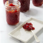 Tomato preserves on a spoon next to a jar of more jam.